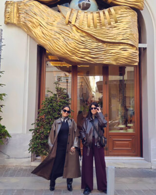 Έλενα και Ιωάννα μπροστά σε χριστουγεννιάτικη βιτρίνα στην Αθήνα με γκαμπαρντίνες, τσόκερ και statement κοσμήματα.