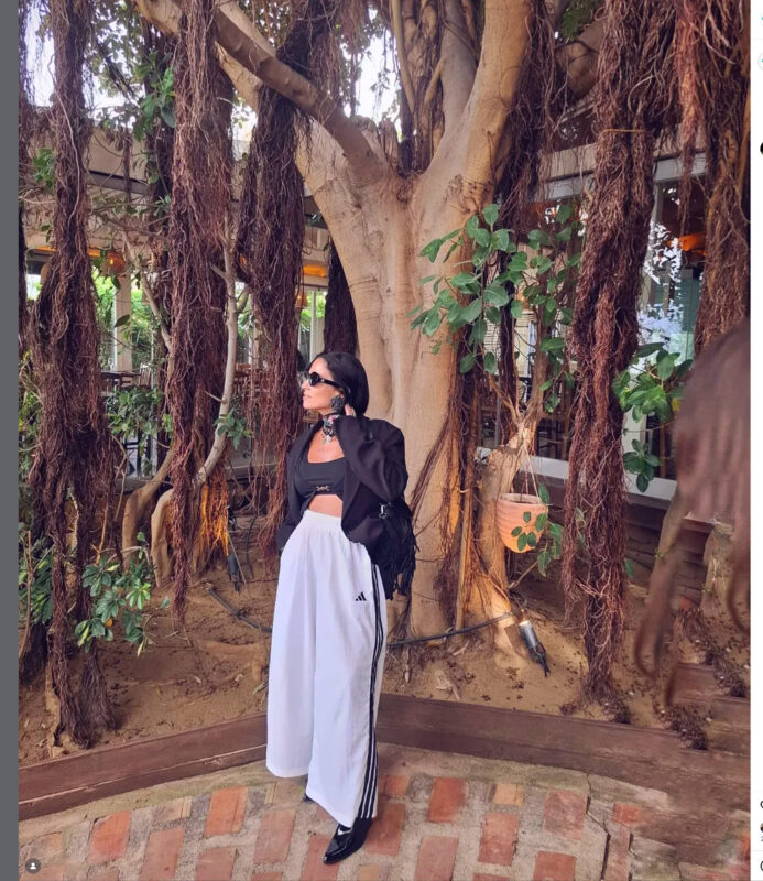 Γυναίκα με μαύρο σακάκι, crop top και λευκή φόρμα σε urban σκηνικό, φορά μεγάλα clip-on σκουλαρίκια.