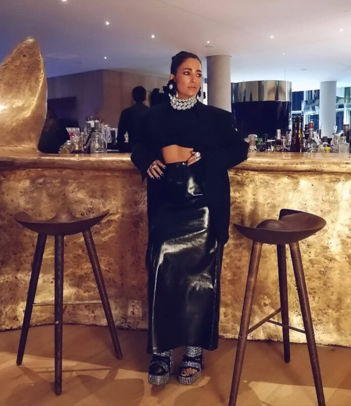 Γυναίκα με total black outfit και statement τσόκερ σε elegant dinner στο εστιατόριο Δέλτα του ΚΠΙΣΝ μπροστά από χρυσό bar.