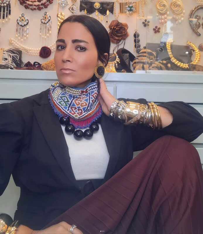 Γυναίκα με πολύχρωμο τσόκερ και μαύρο κολιέ σε layering μπροστά από βιτρίνα με κοσμήματα.