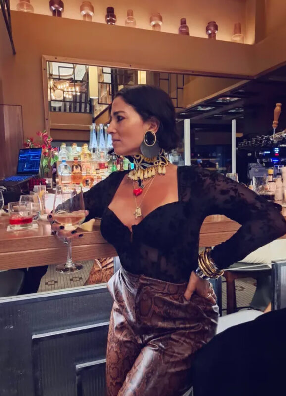 Γυναίκα σε cocktail bar με μαύρη δαντέλα, snakeskin παντελόνι, statement τσόκερ και μεγάλα σκουλαρίκια