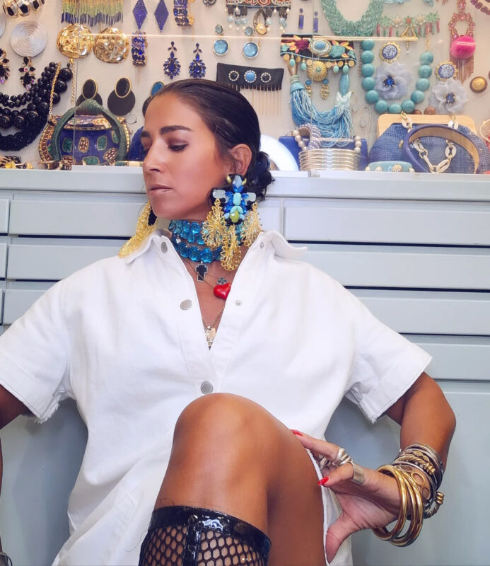 Γυναίκα με λευκό πουκάμισο-φόρεμα, μπλε statement τσόκερ, maxi μπλε-χρυσά σκουλαρίκια και πολλά βραχιόλια.