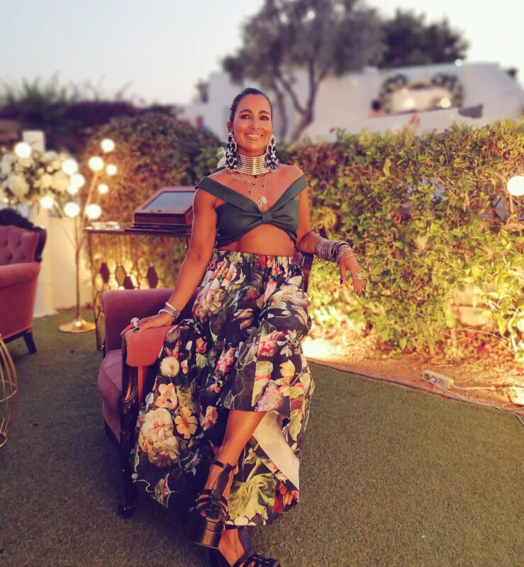 Καλοκαιρινή βραδινή έξοδος με τσόκερ, floral μάξι φούστα, statement σκουλαρίκια και πολλά βραχιόλια σε φωτισμένο κήπο.