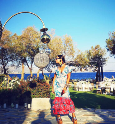 Island Athens Riviera Resort look με printed φόρεμα, statement τσόκερ, μεγάλα σκουλαρίκια και βραχιόλια δίπλα στη θάλασσα.