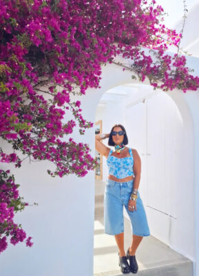 Γυναίκα με denim βερμούδα, γαλάζιο cropped top, statement λαιμό και μεταλλικά βραχιόλια σε καλοκαιρινό maximal look.