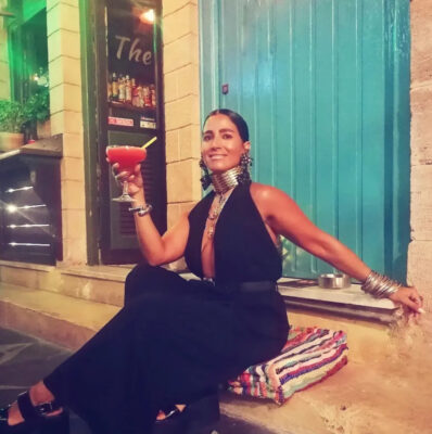 Γυναίκα σε βραδινή cocktail έξοδο με total black outfit, μεγάλο μεταλλικό τσόκερ, μαύρα statement σκουλαρίκια, layered κολιέ και πολλά βραχιόλια.