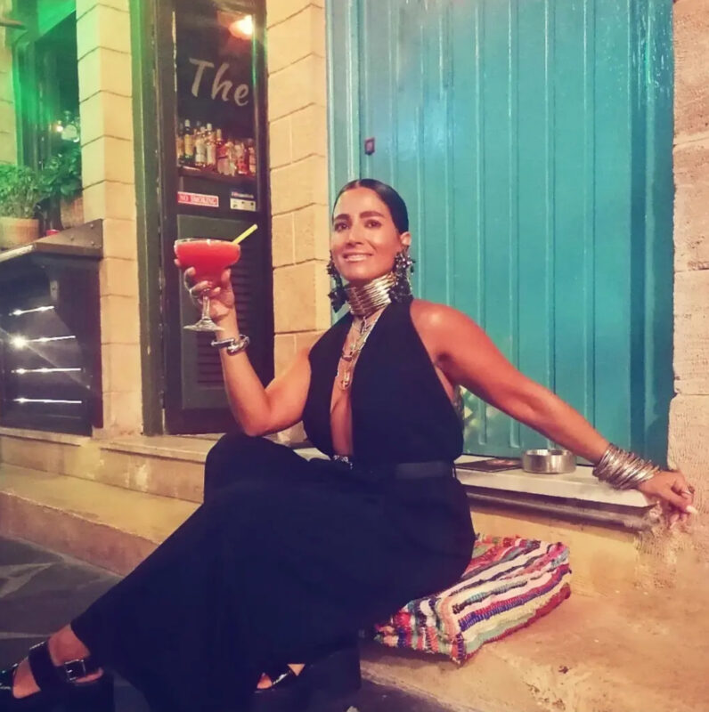 Γυναίκα σε βραδινή cocktail έξοδο με total black outfit, μεγάλο μεταλλικό τσόκερ, μαύρα statement σκουλαρίκια, layered κολιέ και πολλά βραχιόλια.