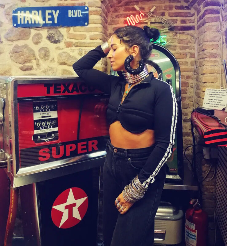 Γυναίκα με total black look, statement μαύρα σκουλαρίκια, μεταλλικό τσόκερ και stacked βραχιόλια σε βραδινό styling.