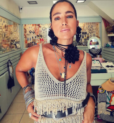 Γυναίκα μέσα στο κατάστημα Double Trouble στην Πάτρα με cream πλεκτό top, μεγάλα μαύρα floral σκουλαρίκια, choker, layered κολιέ και πολλά βραχιόλια.