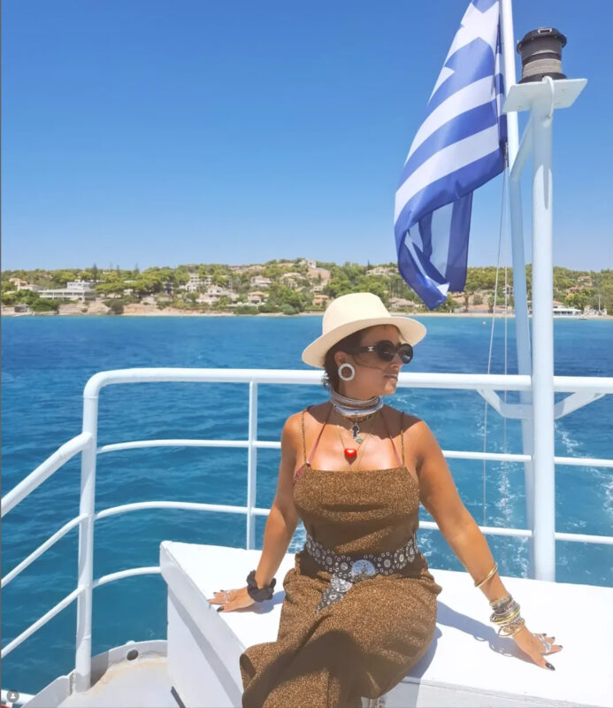 Γυναίκα με ψάθινο καπέλο, μεταλλικό τσόκερ, vintage belt, statement σκουλαρίκια και λαμπερό φόρεμα σε καλοκαιρινό look.