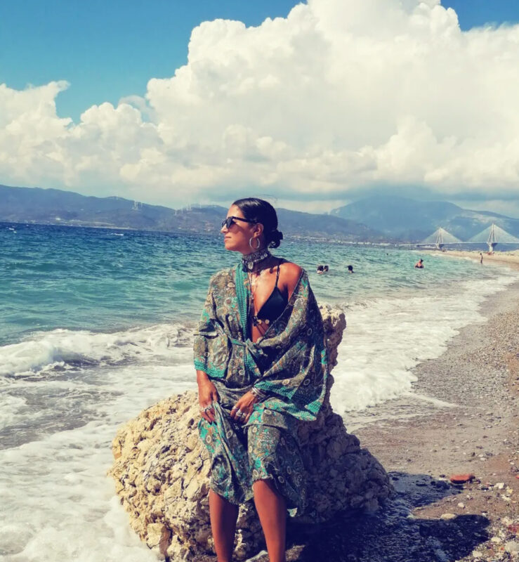Γυναίκα με boho καλοκαιρινό look στην παραλία, τσόκερ, layered κολιέ και μεταλλικά βραχιόλια.