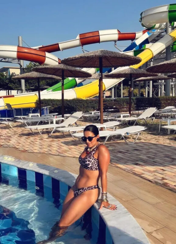 Γυναίκα με leopard bikini, statement κολιέ, πολλά βραχιόλια και γυαλιά ηλίου δίπλα σε πισίνα και νεροτσουλήθρες water park.