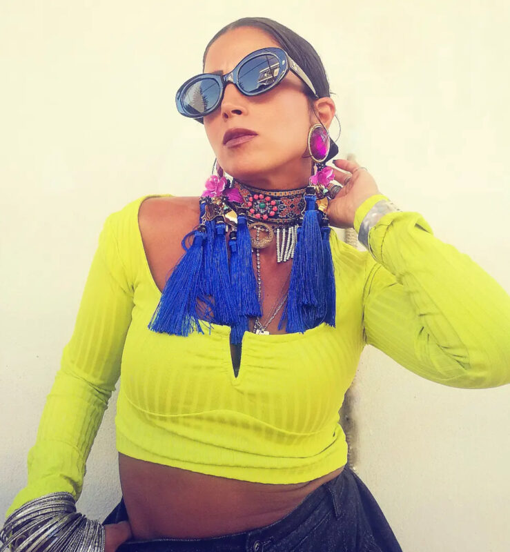 Γυναίκα με neon lime top, πολύ μεγάλα μπλε σκουλαρίκια με φούντες, πολύχρωμο τσόκερ, oversized γυαλιά και πολλά ασημί βραχιόλια.