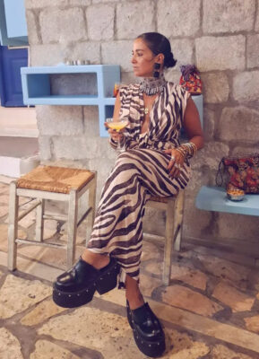 Γυναίκα με zebra print καλοκαιρινό outfit, μεγάλο μεταλλικό statement choker, μαύρα σκουλαρίκια, πολλά βραχιόλια και μαύρα platform παπούτσια.