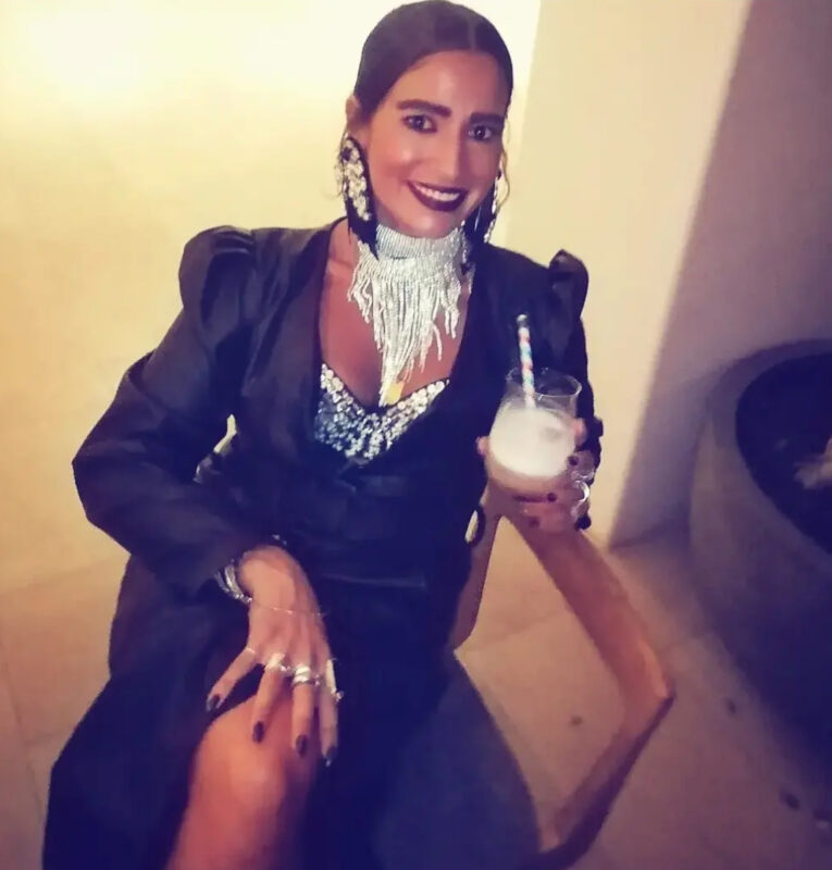 Γυναίκα με μαύρο βραδινό outfit, ασημί τσόκερ με μακριά μεταλλικά κρόσσια, μεγάλα μαύρα σκουλαρίκια, κρυστάλλινο bralette και πολλά δαχτυλίδια.