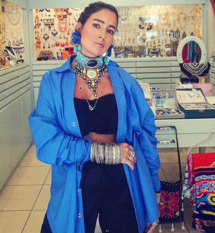 Γυναίκα στο κατάστημα Double Trouble στην Πάτρα με έντονο μπλε oversized πουκάμισο, πολύχρωμο τιρκουάζ τσόκερ, μεγάλα σκουλαρίκια, layered κολιέ και πολλά μεταλλικά βραχιόλια.